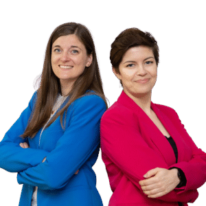 Daria i Kinga oparte o siebie plecami, uśmiechają się. Daria jest ubrana w marynarkę w kolorze chabrowym, a Kinga w jaskrawo różową.